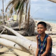 A boy sits in one of the broken coconut trees along the shore